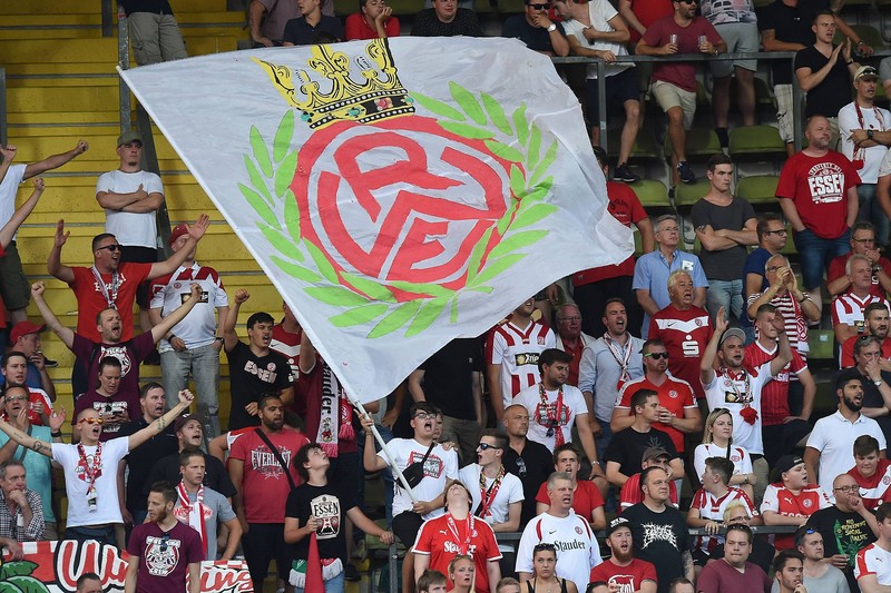 Treue Fans des Rot-Weiß Essen jubeln ihrer Mannschaft mit der Vereinsfahne zu.